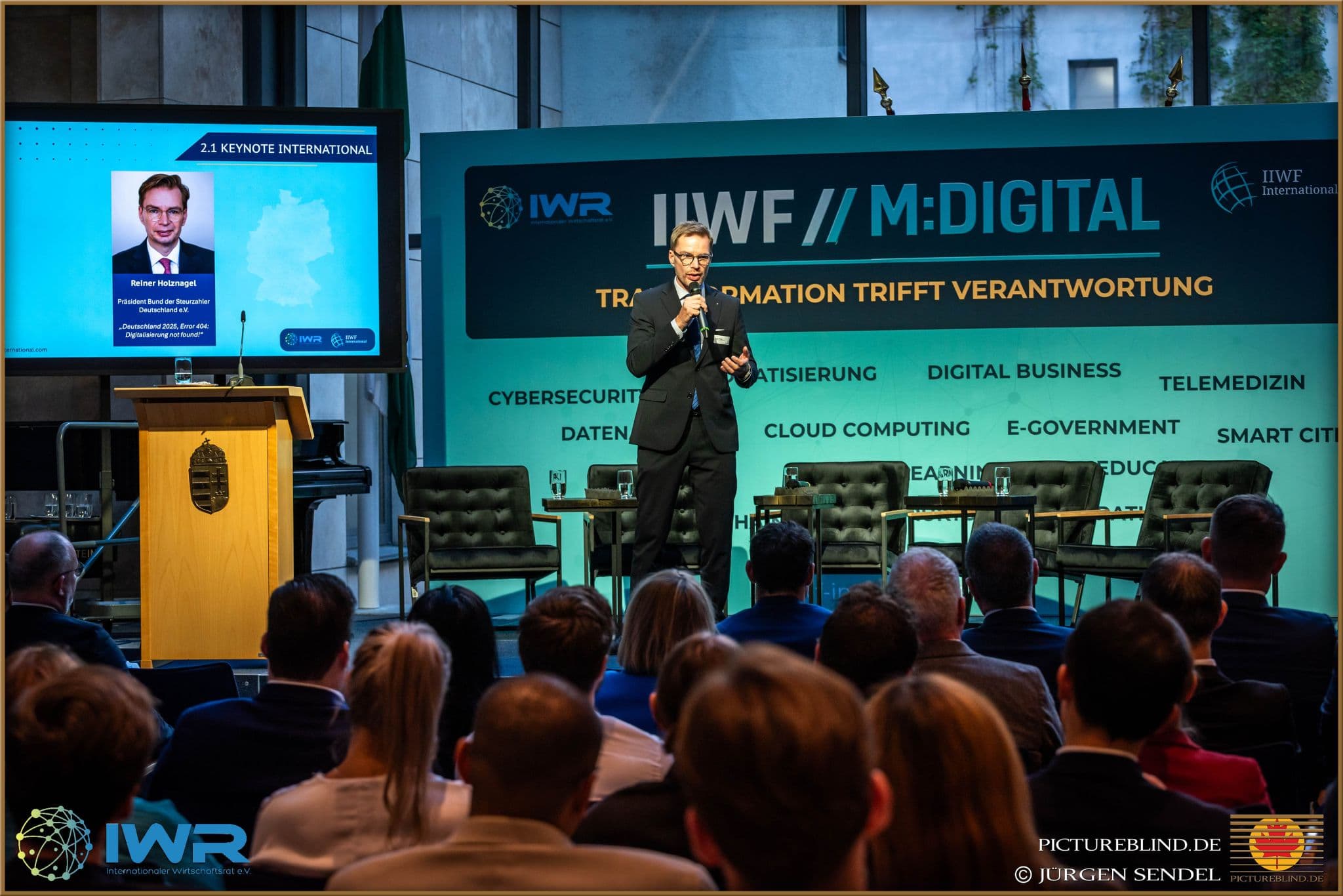 Keynote auf der Bühne vor dem Bühnenbild „IIWF // M:DIGITAL“.